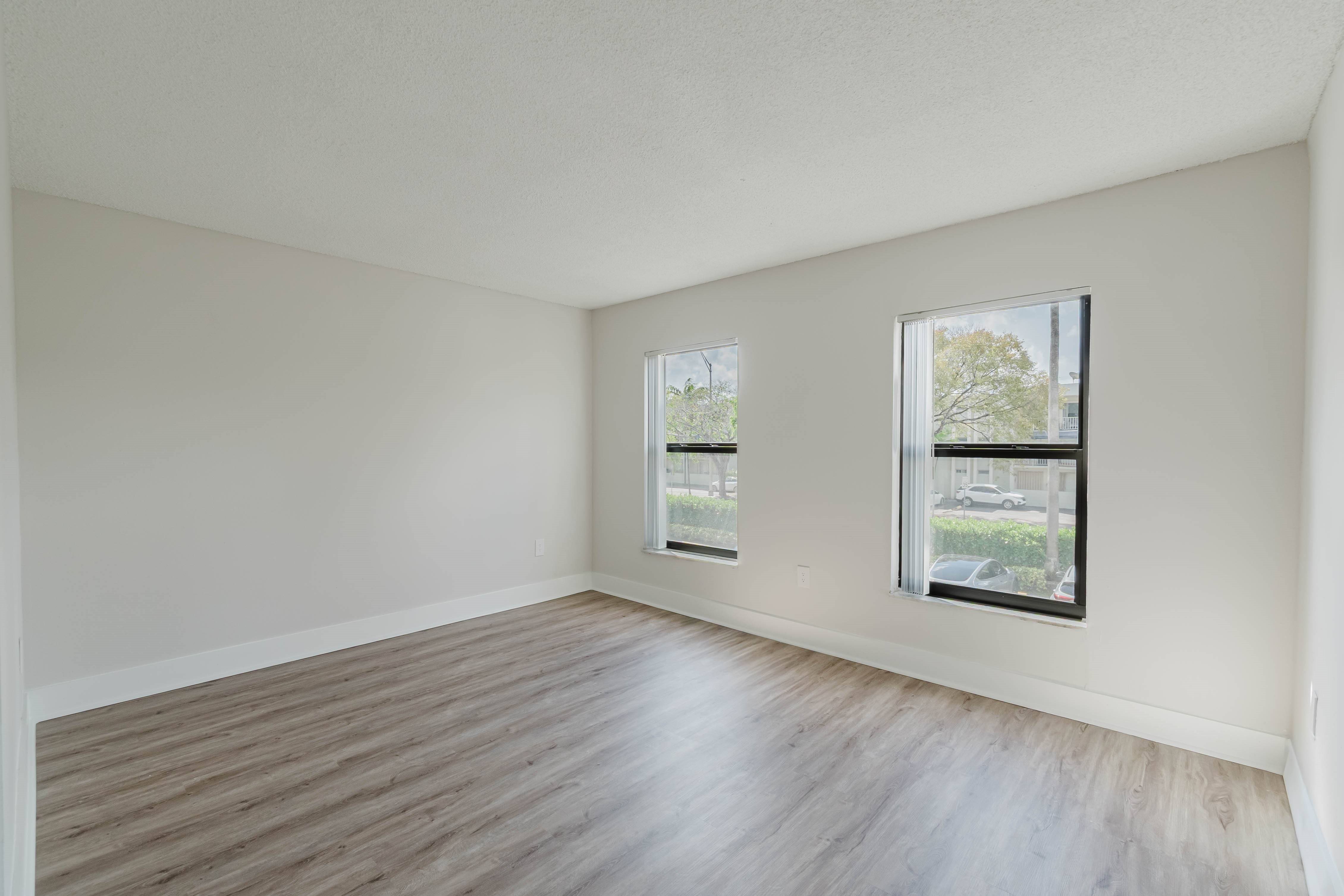 A room with wooden flooring and two windows.